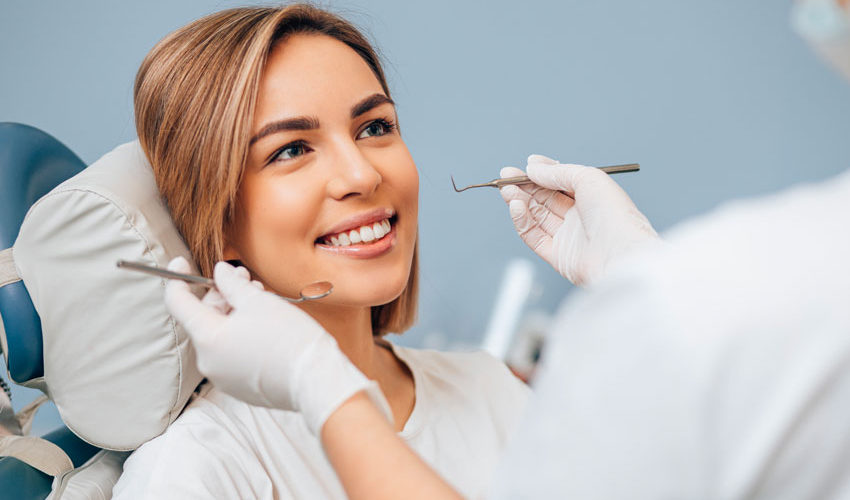 Woman receiving dental examination in bright clinic room with dentist holding mirror.