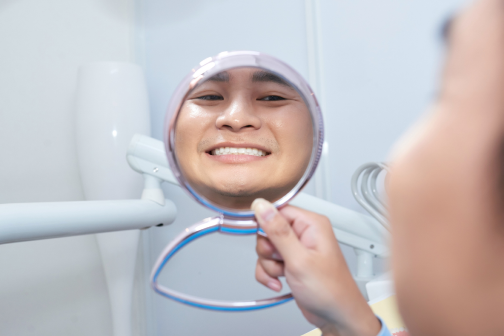 Young patient smiling at dental mirror during examination in modern dental office setting.