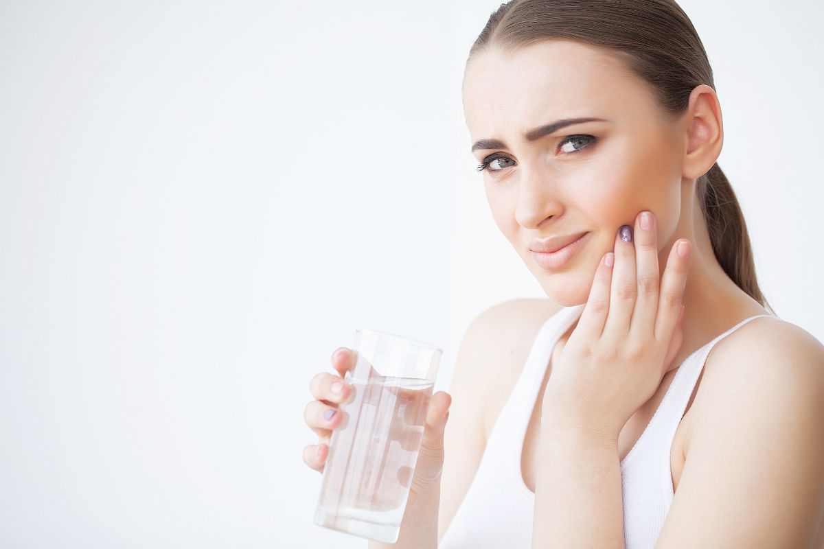 A woman experiencing tooth sensitivity while holding a glass of water illustrates a common warning sign of dental cavities.
