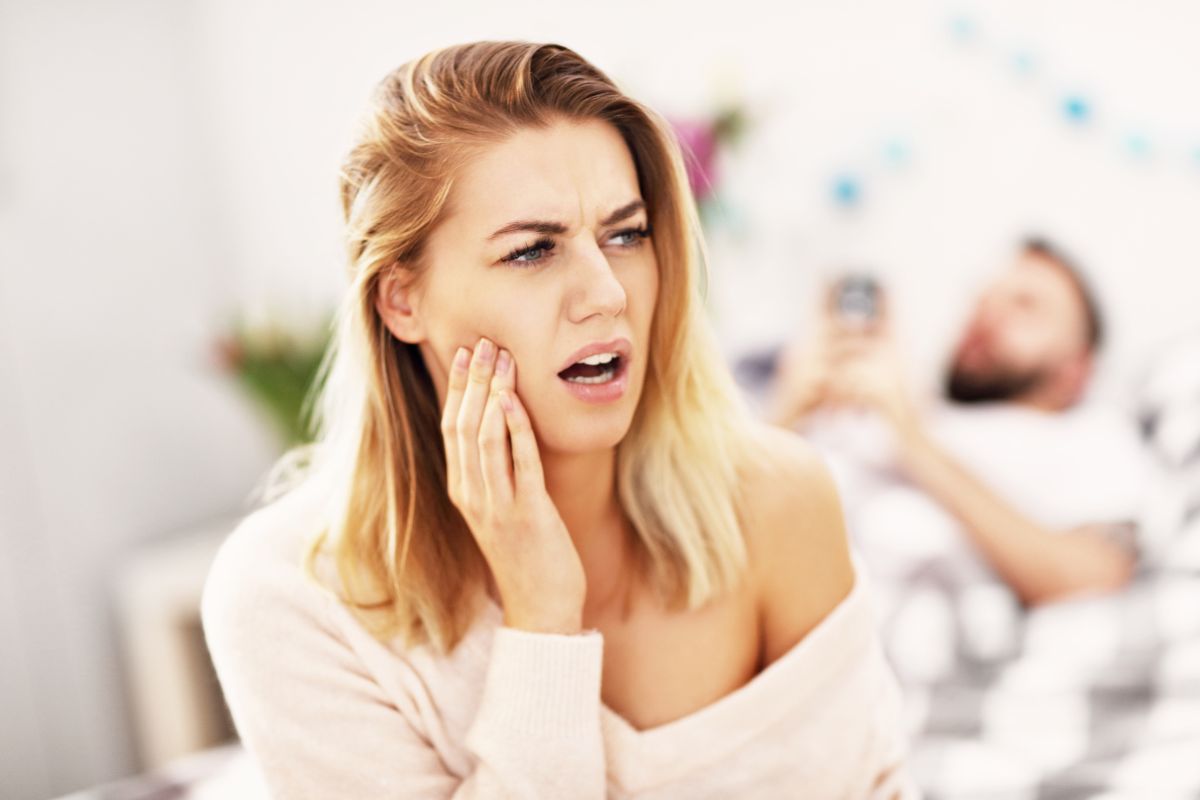 A woman holding her cheek in discomfort at home represents the frustration and pain that can accompany untreated toothaches.