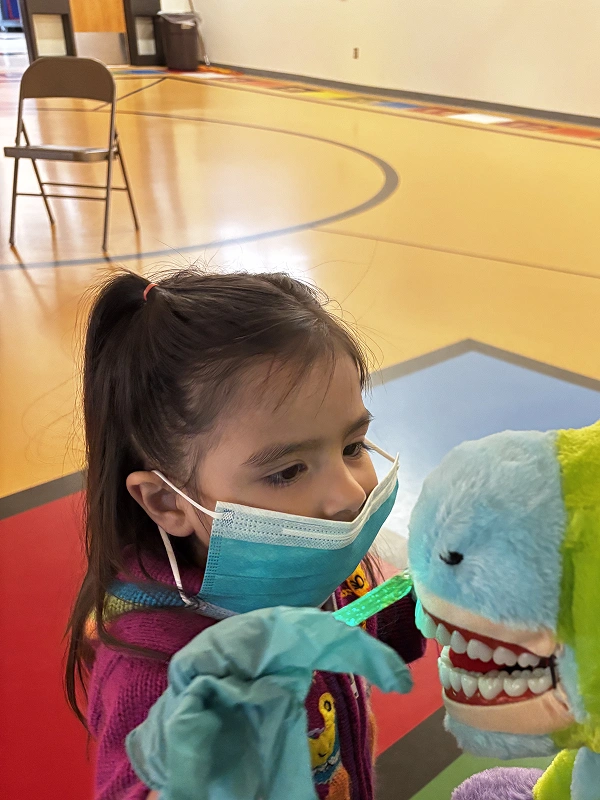 Child practicing dental hygiene with a puppet at a Smile Xpressions Dentistry community event